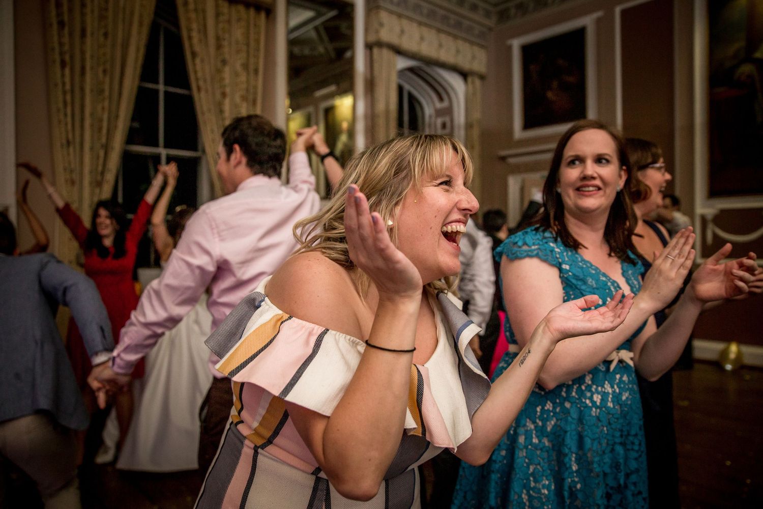Wedding reception dance floor with guests celebrating in an elegant ballroom with ornate ceiling.