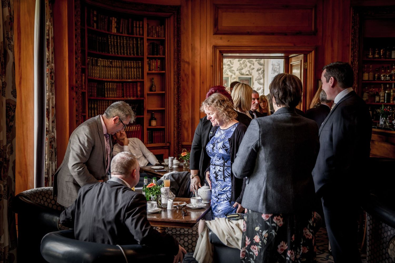 Guests gather in an ornate wood-paneled library during a wedding reception.