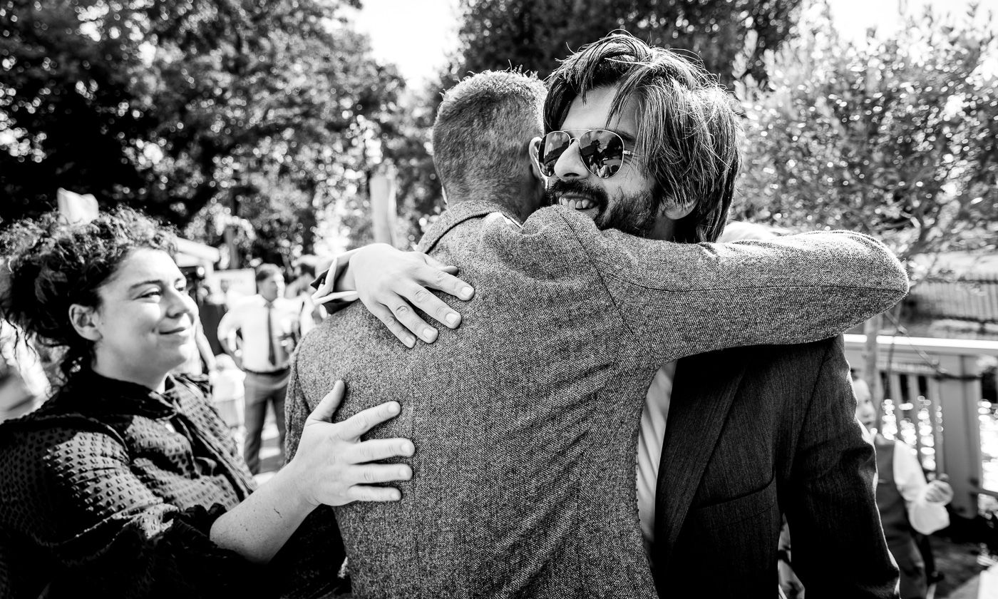 Black and white photograph of wedding guests embracing during an emotional moment.