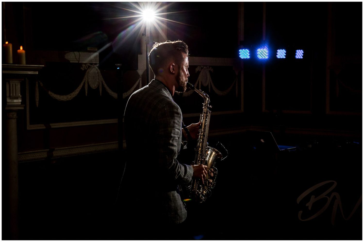 A saxophonist performs in dramatic lighting against a dark background during a jazz performance.
