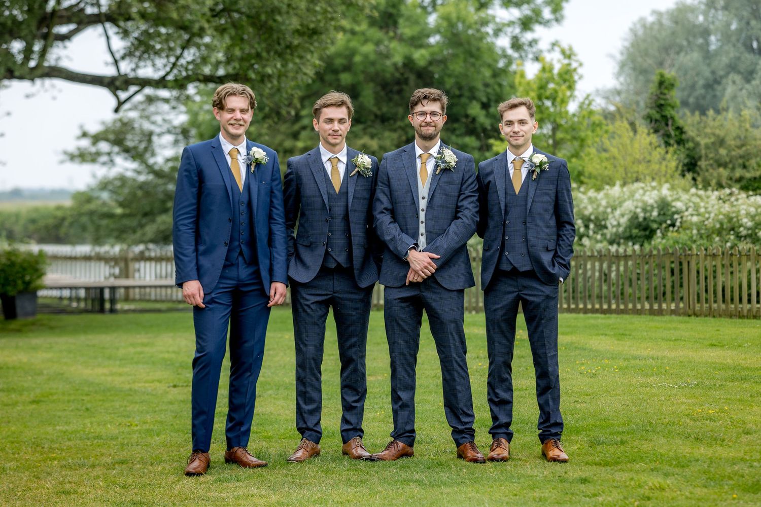 Groomsmen in navy suits pose together on green lawn.