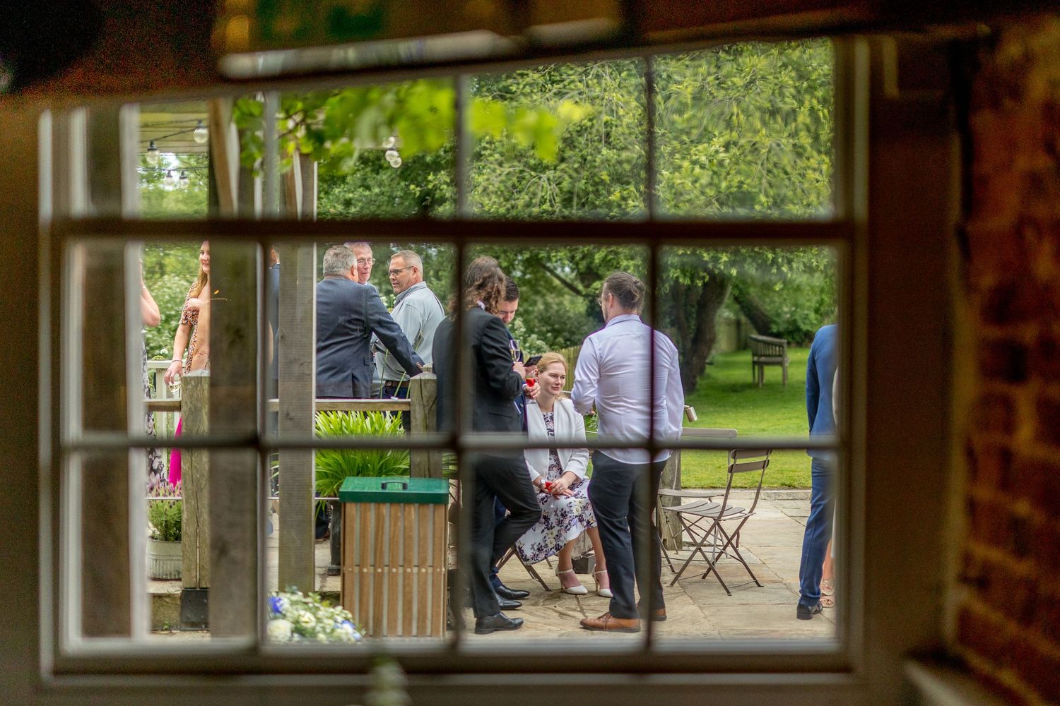 View through rustic window frames of wedding guests gathering in a garden setting.