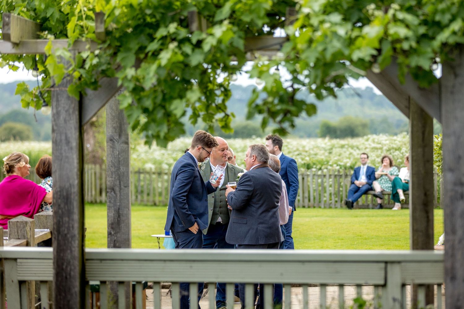 Outdoor wedding reception with guests gathered under wooden pergolas.
