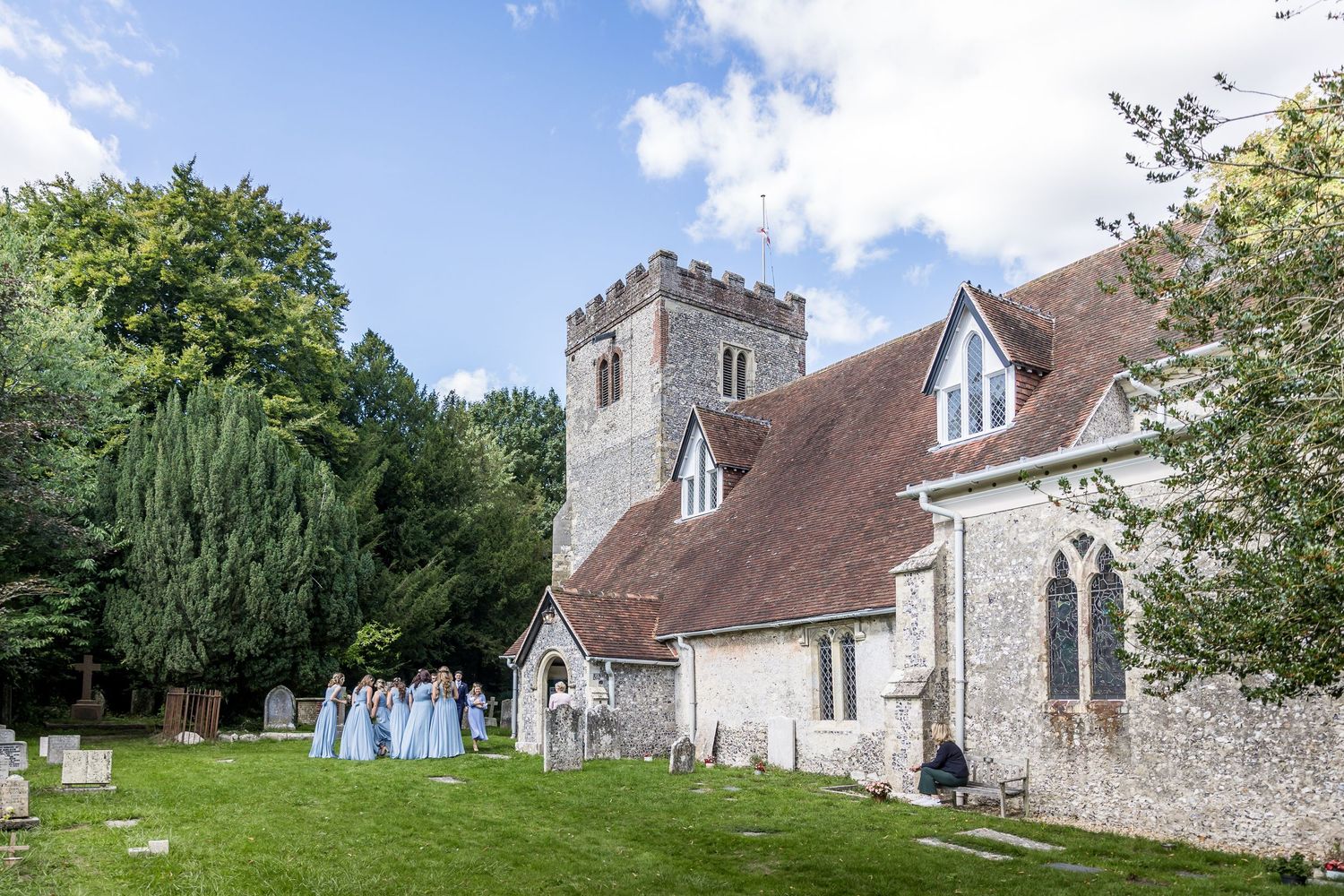 Traditional English stone church exterior with cemetery and rolling hills in background.