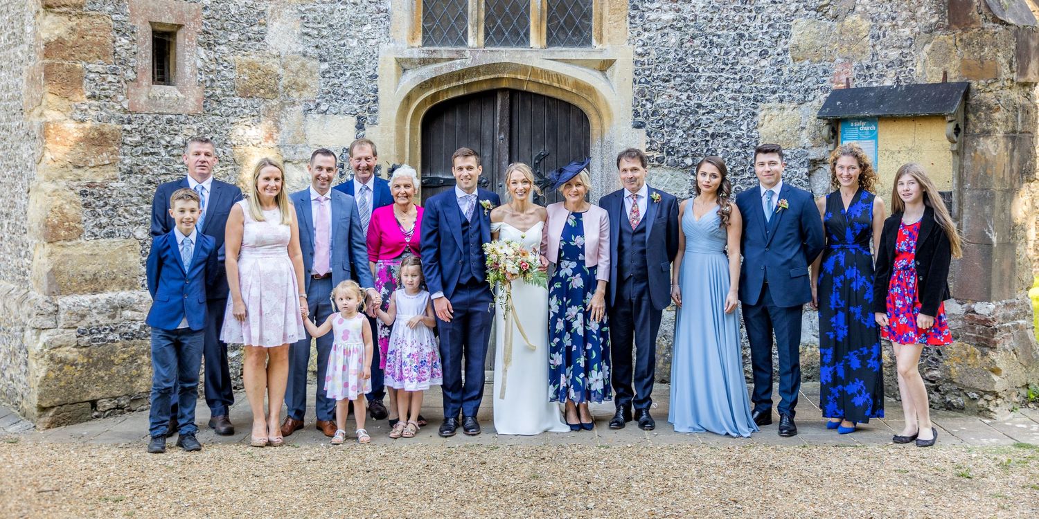 Large group wedding photo in front of a historic stone church with gothic architecture.
