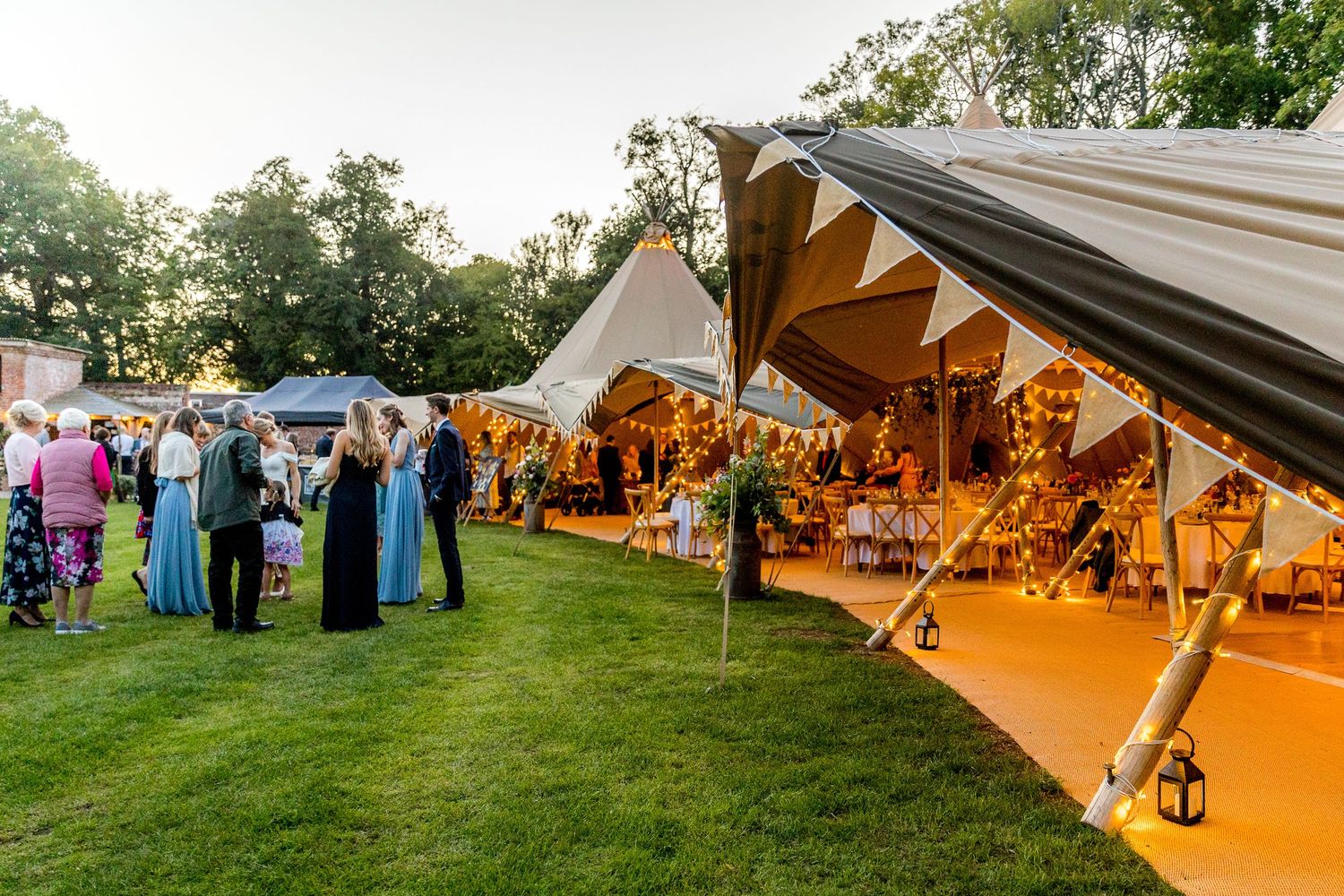 Wedding reception setup with illuminated tipi tents and outdoor seating at dusk.