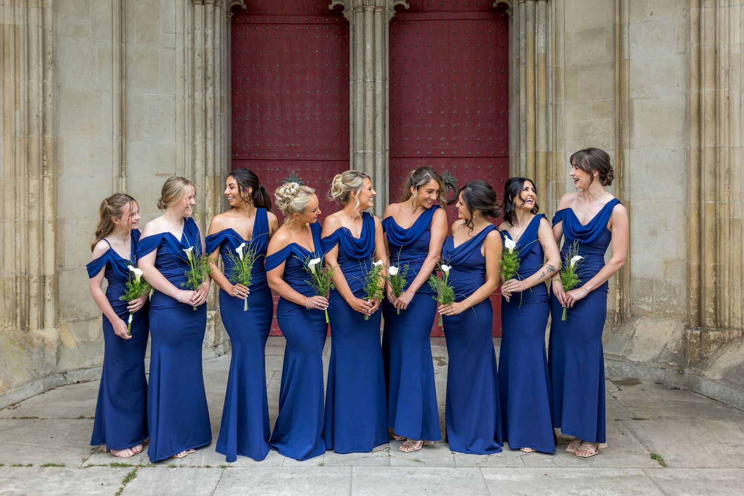 Wedding party in navy blue dresses posed against a stone church exterior.