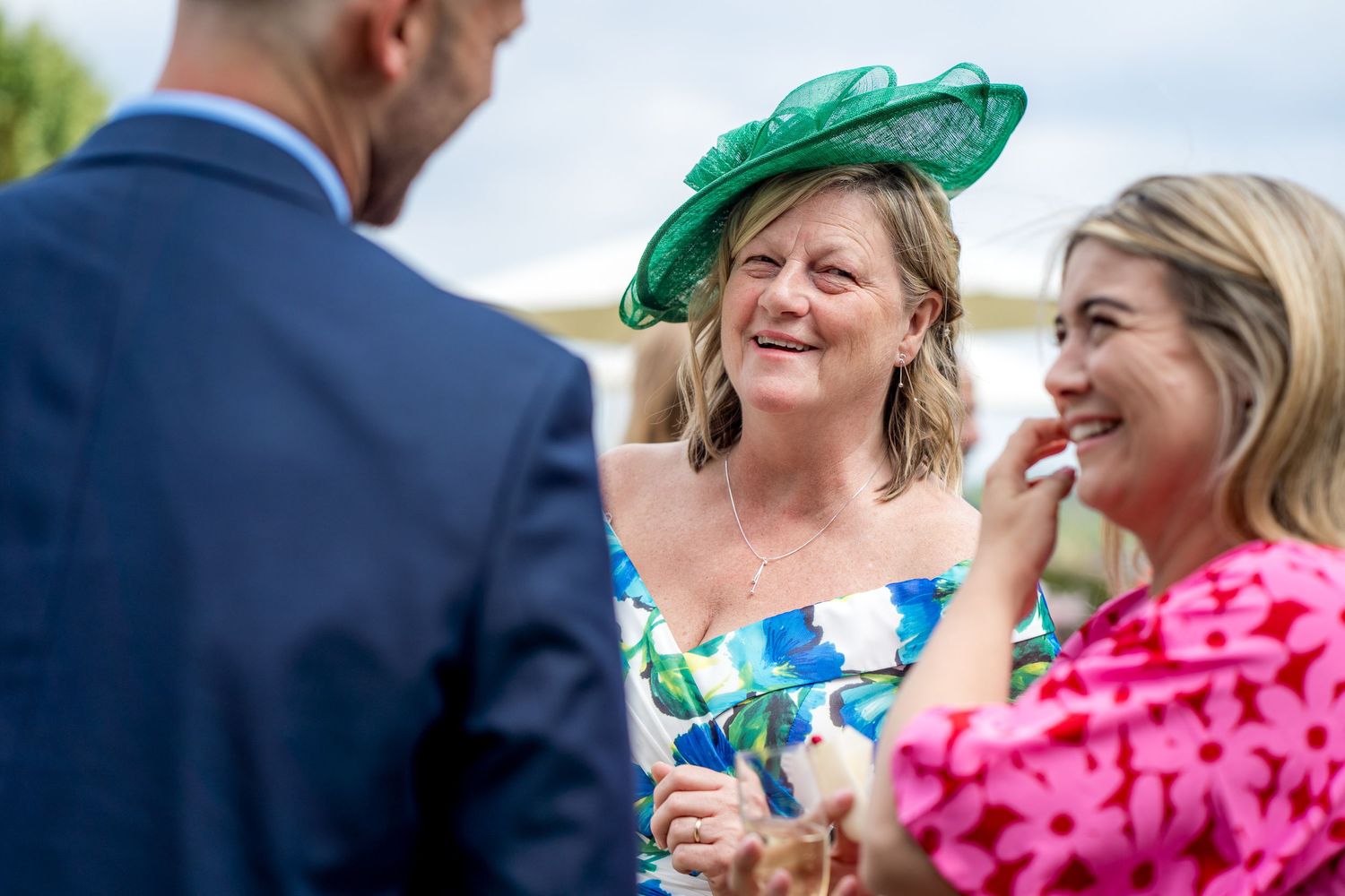 Wedding guests in colorful attire and fancy hats socializing at outdoor reception.