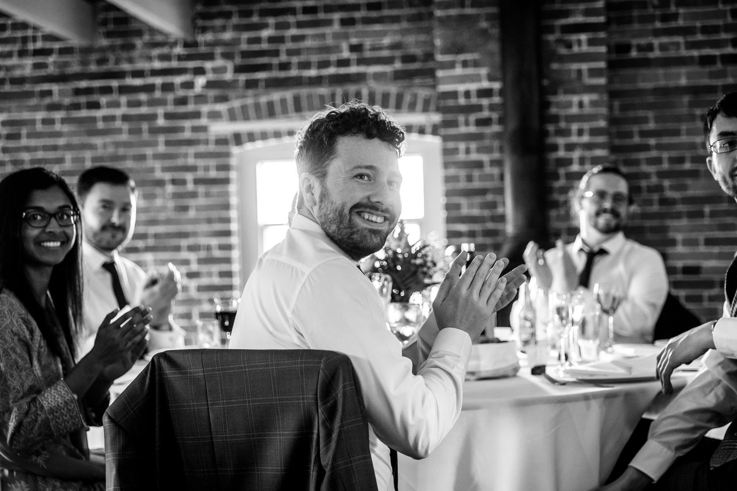 Wedding party enjoying a lively celebration with animated expressions at a brick-walled venue.