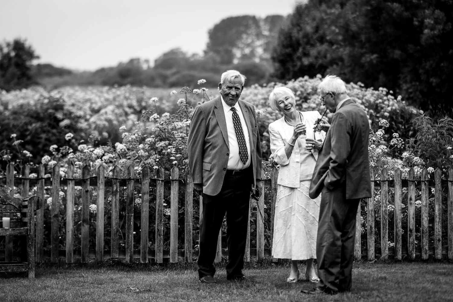 Black and white photo of wedding guests gathered by a wooden fence.