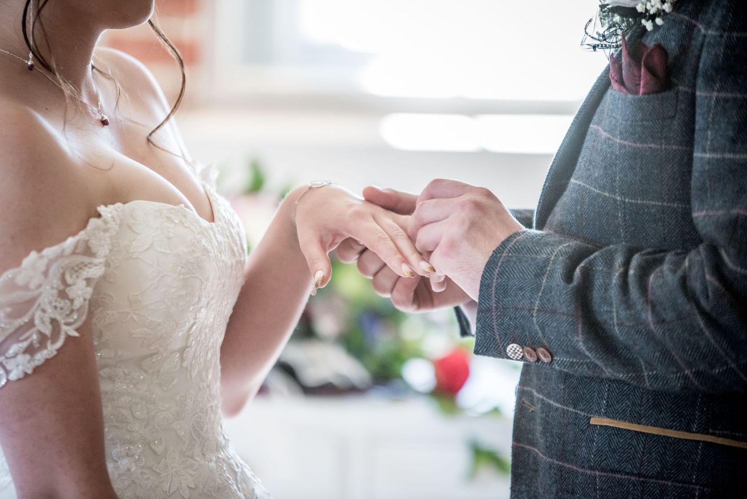 Wedding couple holds hands during ceremony with white and red floral details visible.