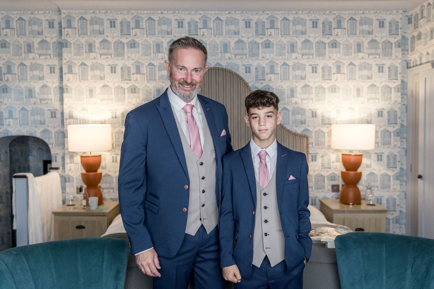 Wedding party members in formal attire posing in front of patterned wallpaper.