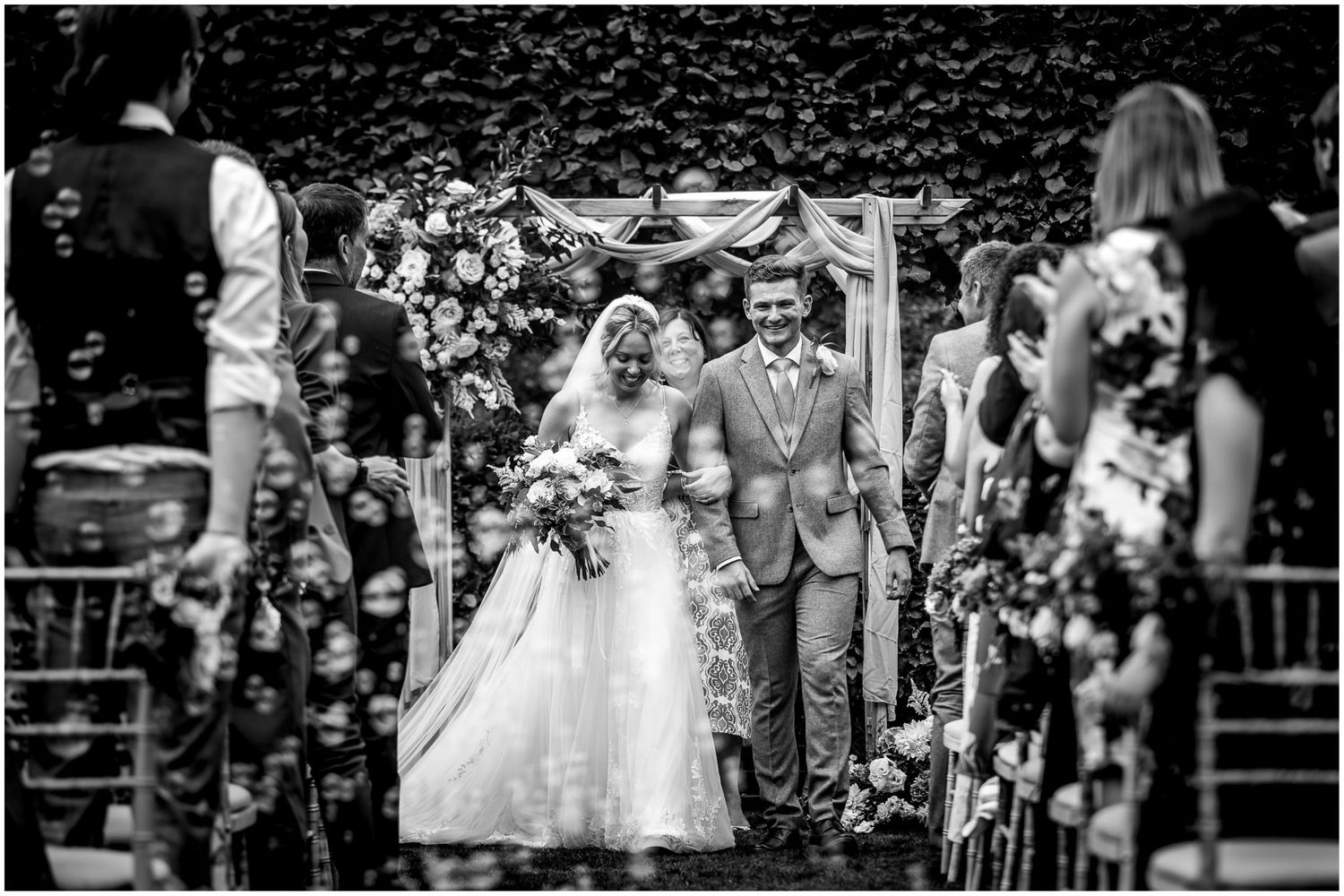 Panoramic view of wedding guests seated in rows during an outdoor garden ceremony.