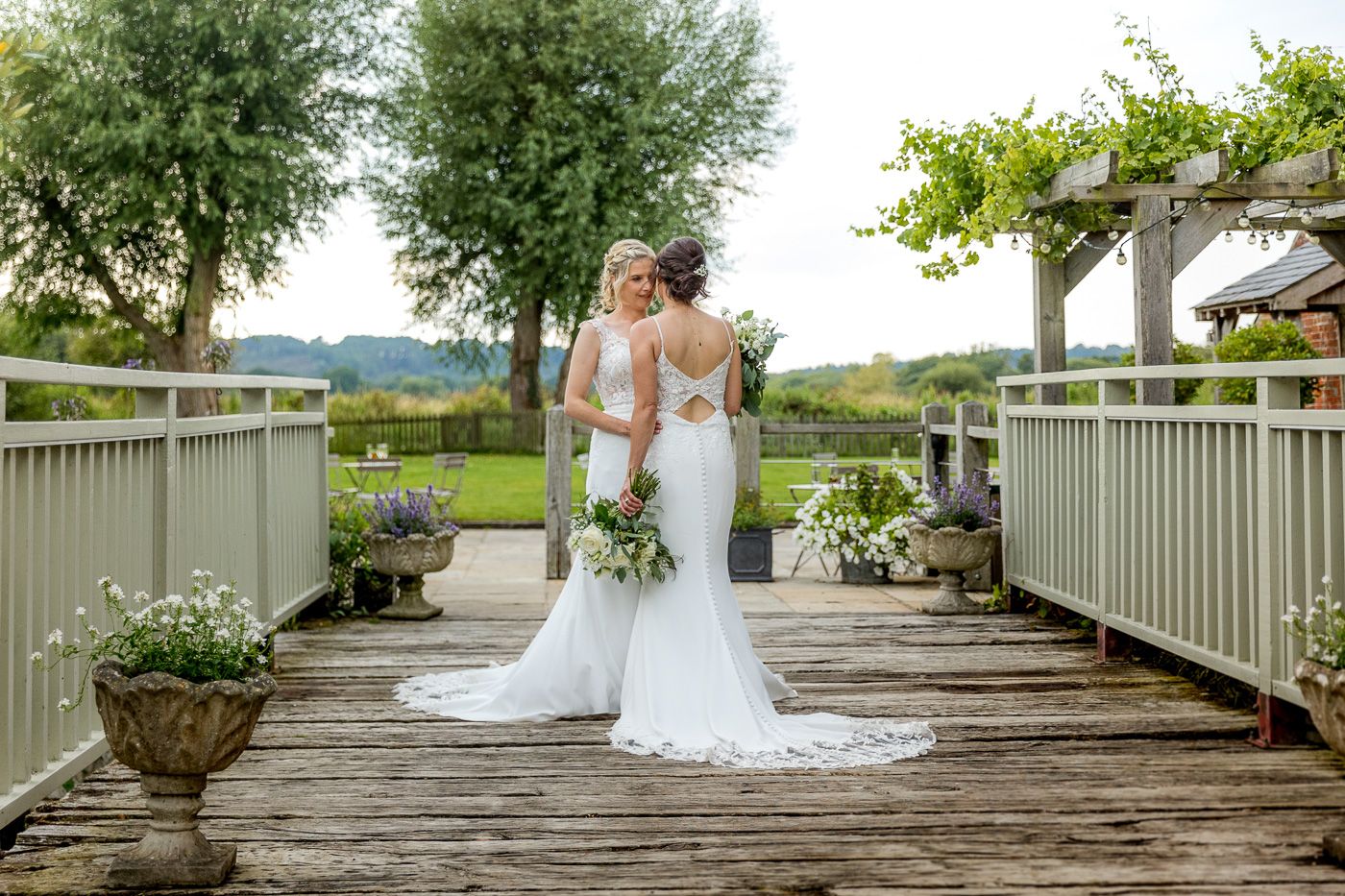 Elegant white wedding dress photographed from behind on a wooden deck overlooking a scenic landscape.