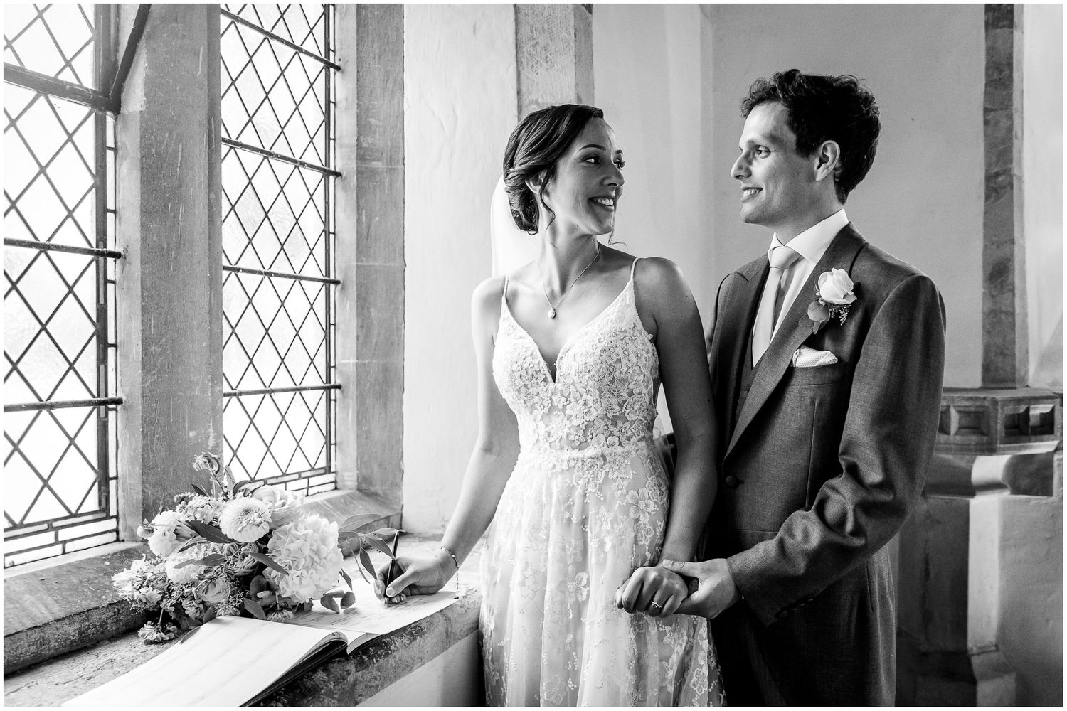 Black and white photo showing a couple in formal attire by church windows.