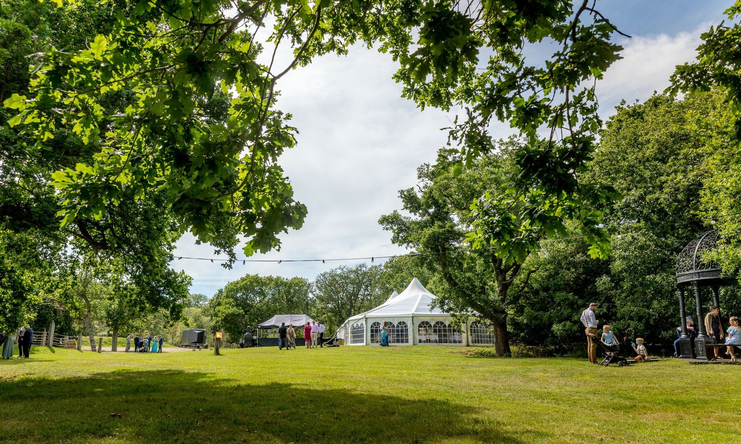 Panoramic view of lush green lawn with white tent and trees on sunny summer day.