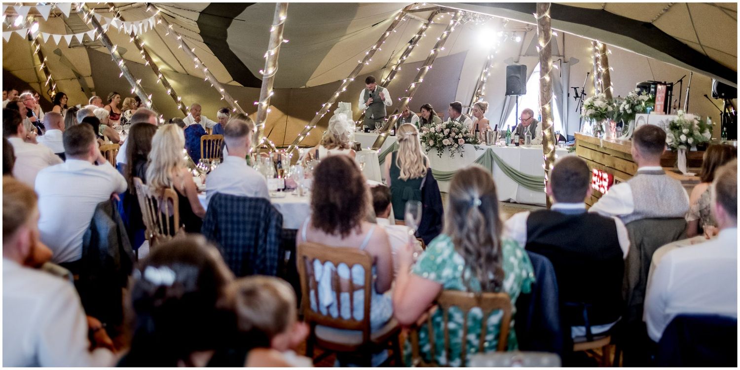 Panoramic view of a wedding reception with guests seated at long tables under twinkling lights.