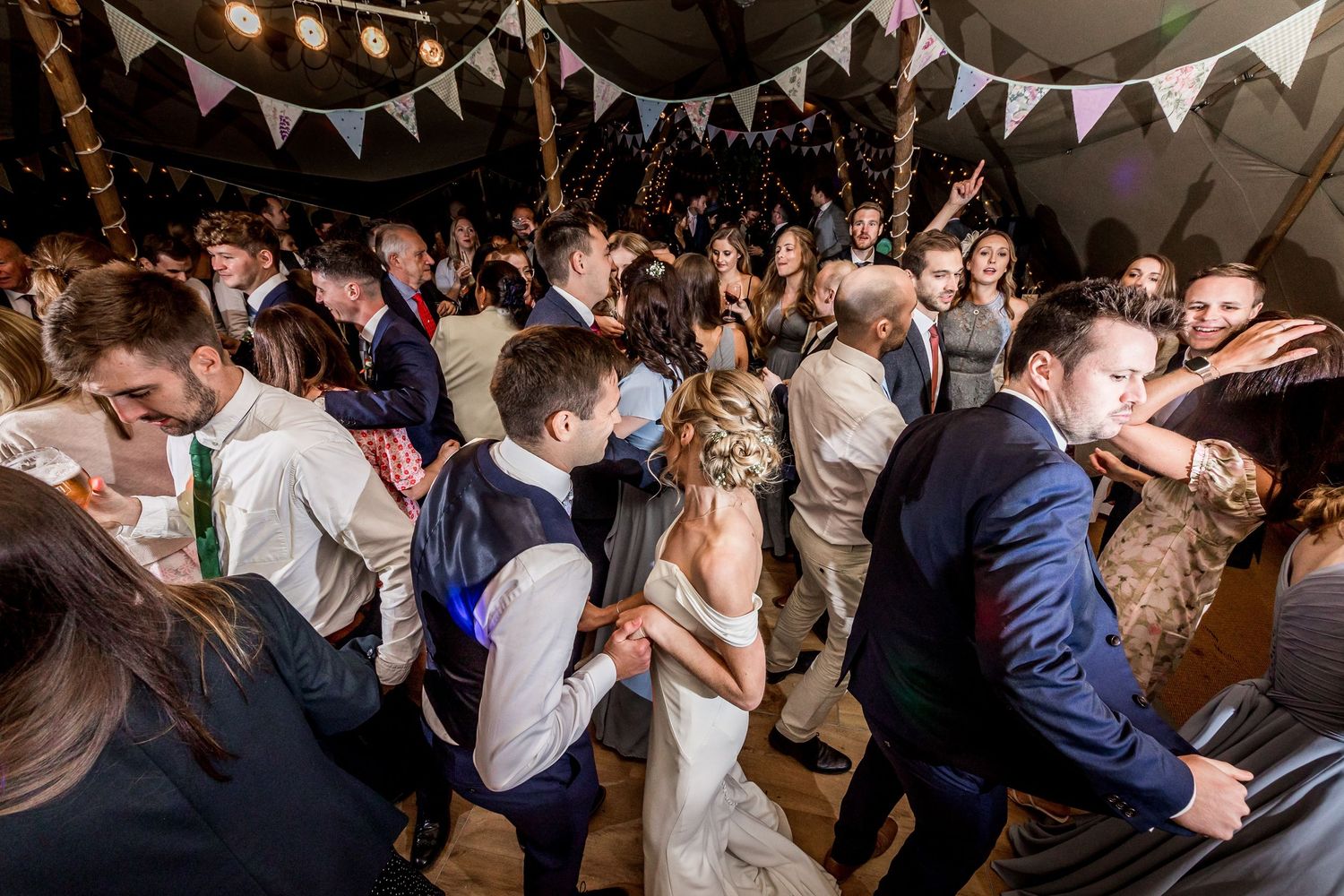 Wedding guests pack the dance floor during a lively reception celebration under string lights and bunting.