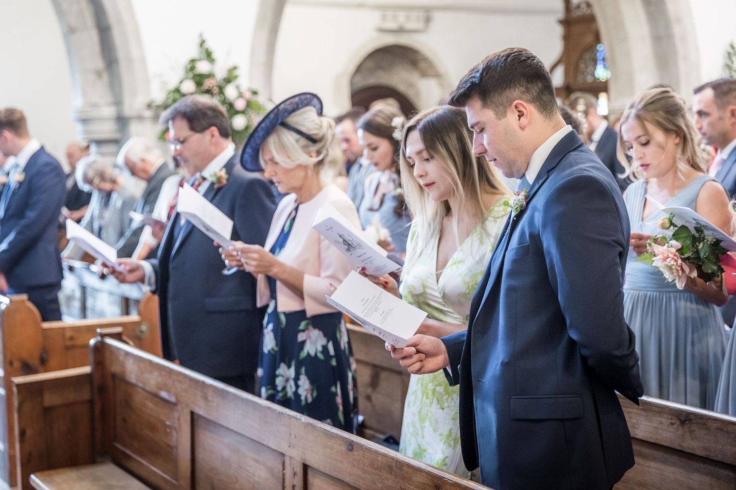 Wedding guests follow along with ceremony programs in traditional church setting.