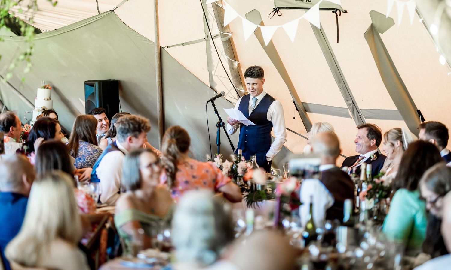 Wedding reception venue with guests seated at decorated tables under tent.