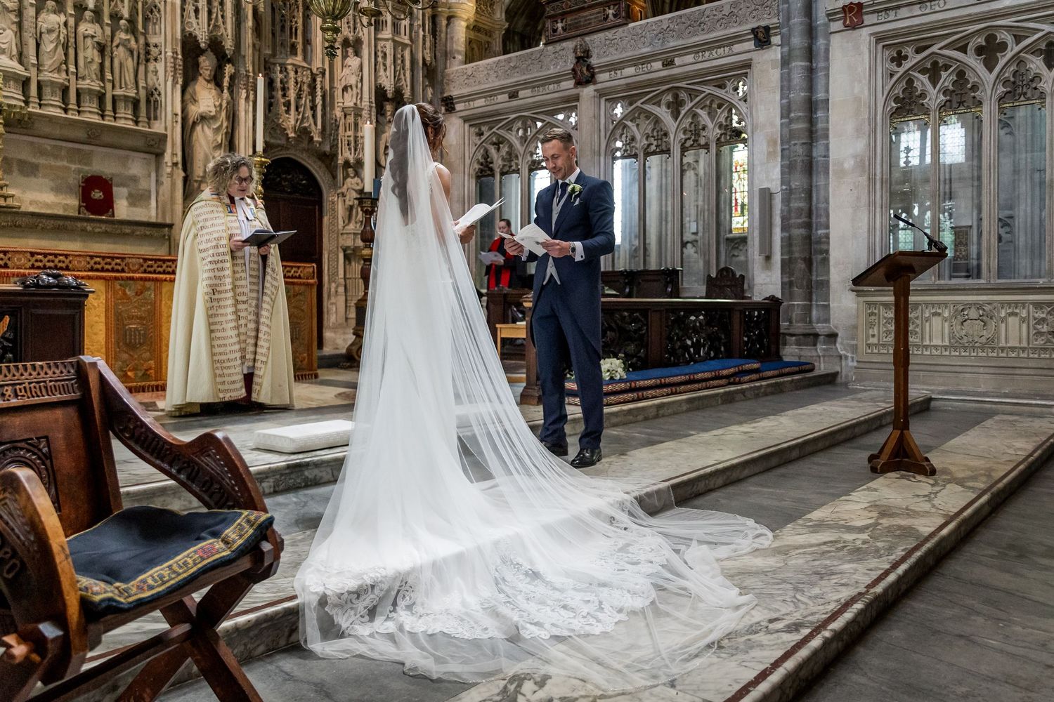 Wedding dress train elegantly trails across stone cathedral floor during ceremony photographs.