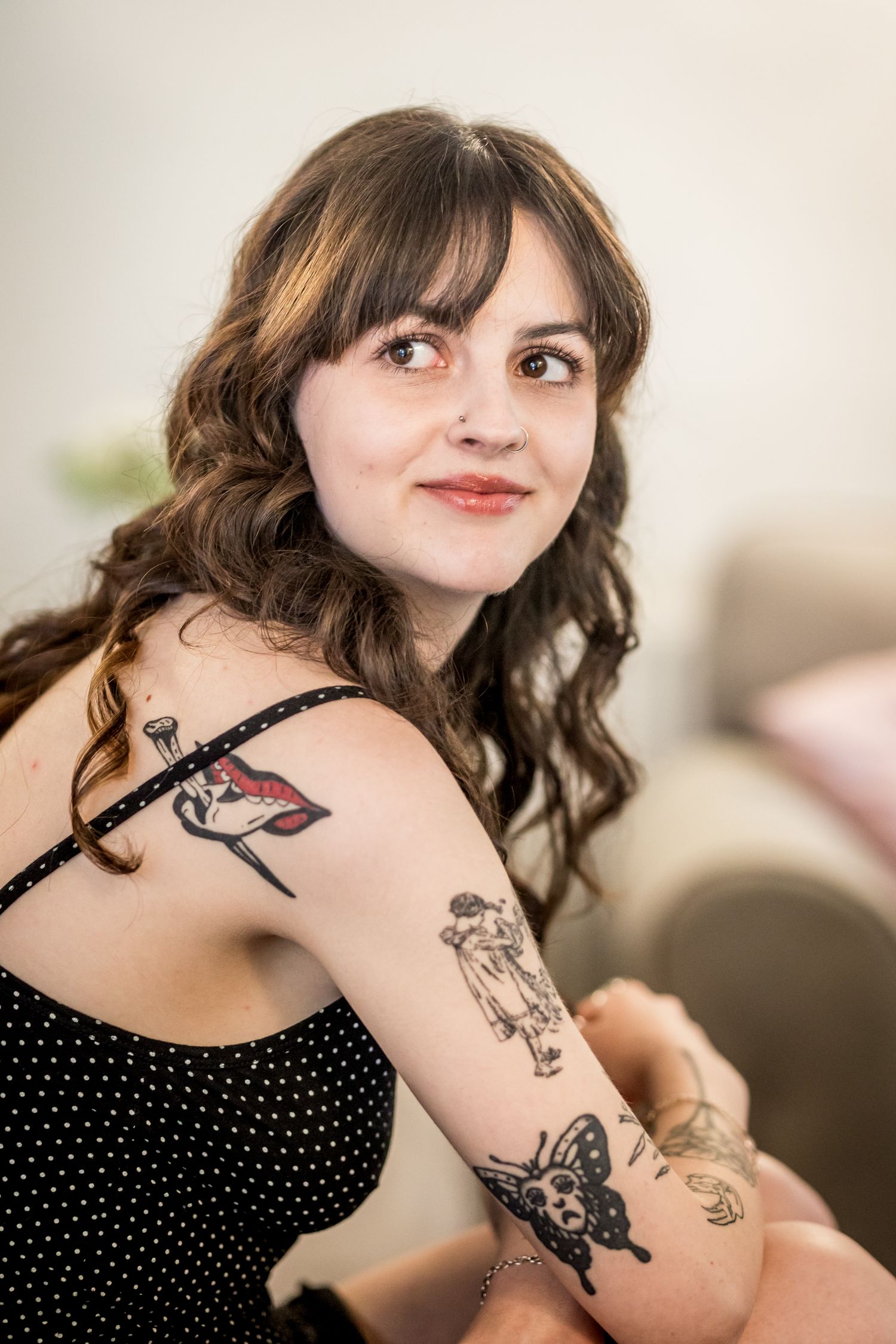 Person in polka dot dress shows artistic tattoos on their arm while seated.