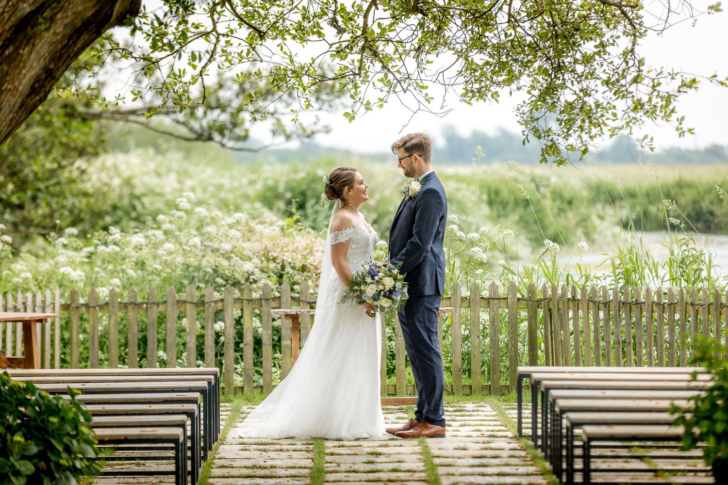 Wedding couple and guests gather on wooden deck overlooking scenic countryside.