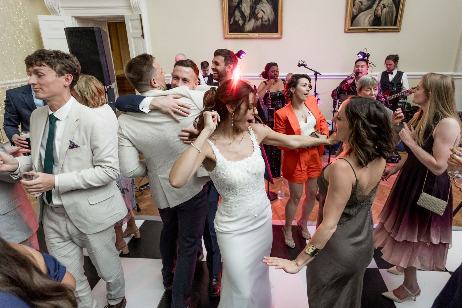 Lively wedding reception with guests dancing and celebrating in an ornate room with classical decor.
