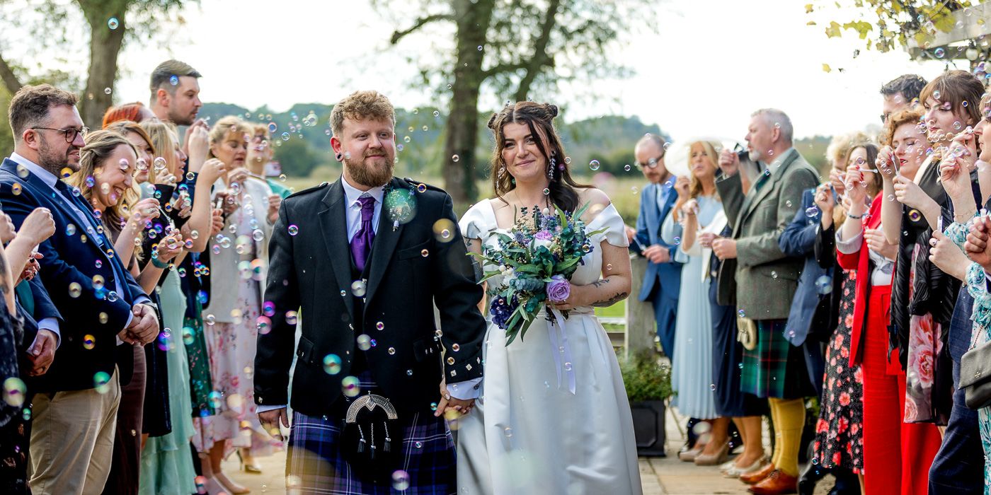 Wedding party celebrating outdoors with confetti and bubbles under green trees.