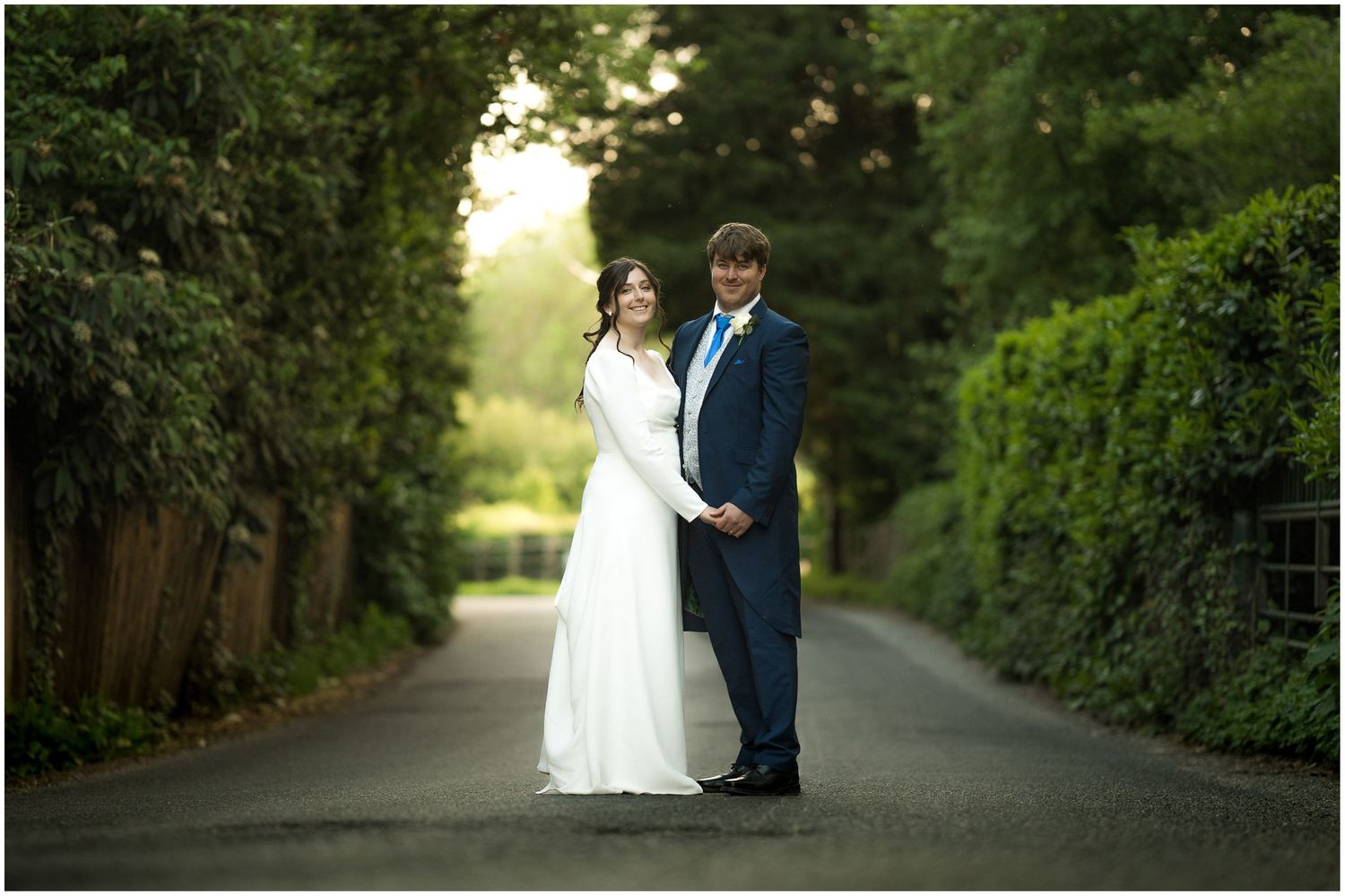 Couple walking along a tree-lined path during their wedding photoshoot.