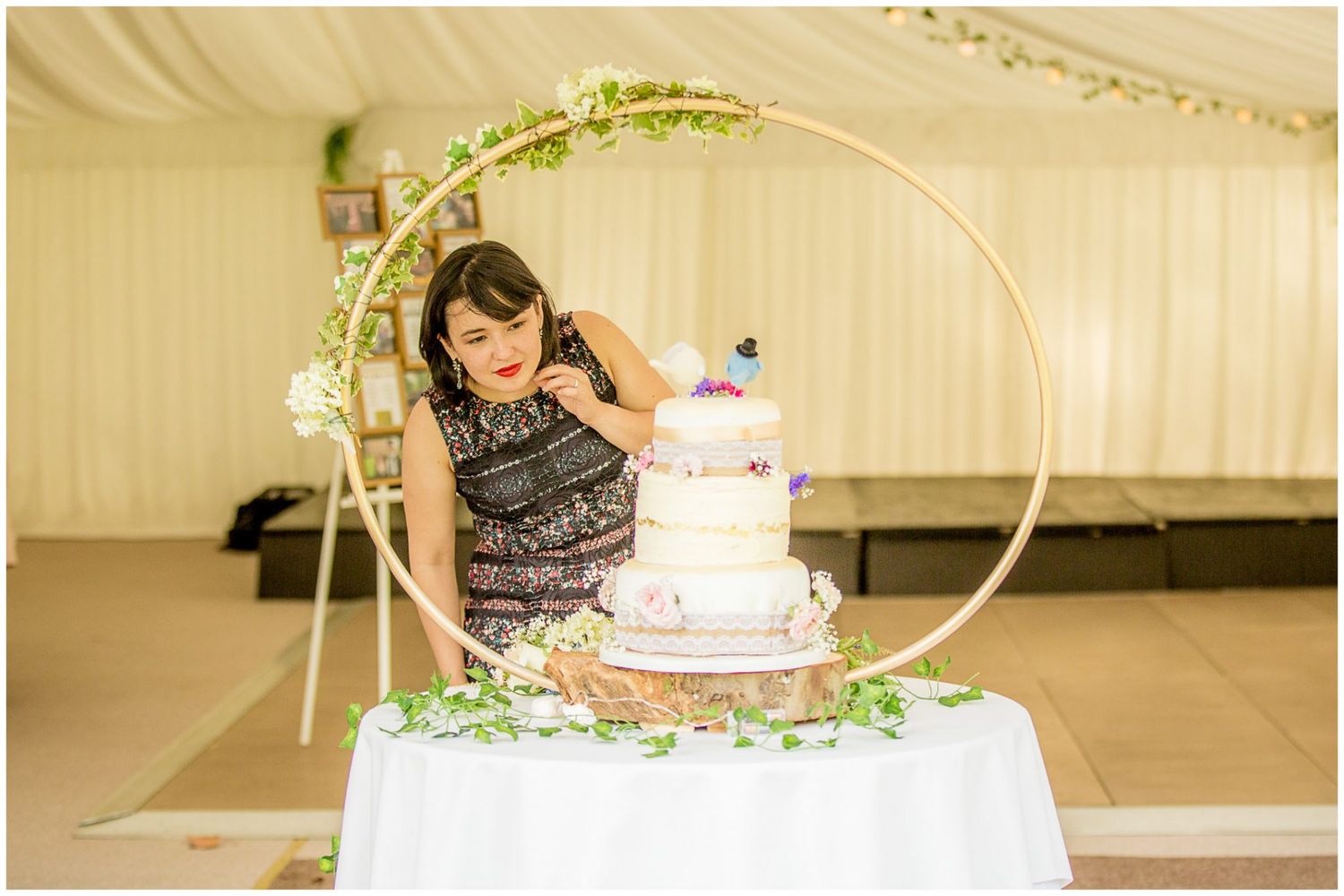 A wedding cake cutting ceremony under a white tent with decorative floral arrangements.