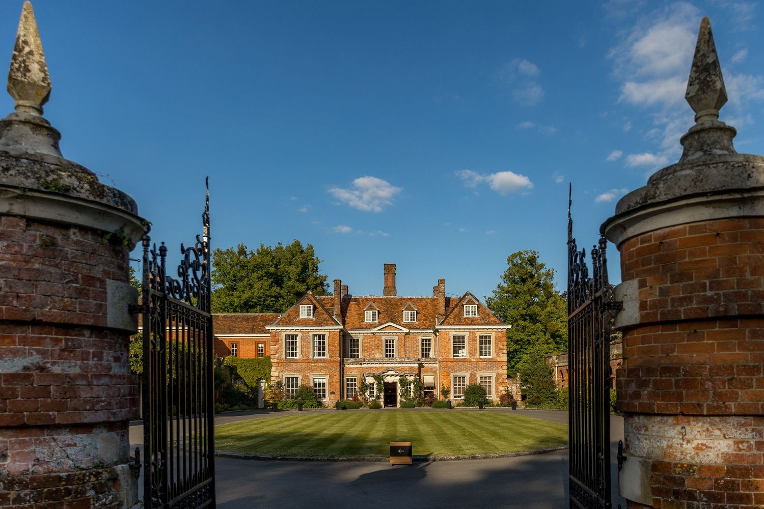 Wide angle exterior shot of a grand Victorian estate with decorative gates and manicured lawns.