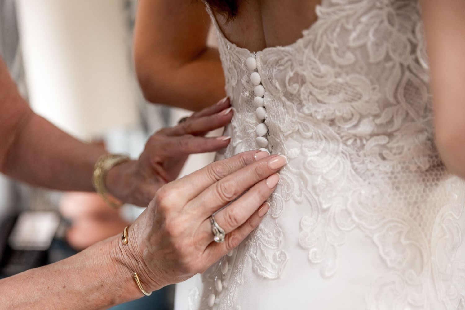 Detail shots of intricate lace wedding dress being fastened.