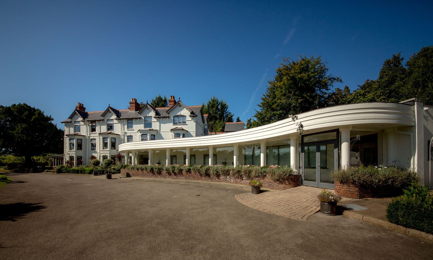 Panoramic view of a stately manor house with white columns and curved driveway on a bright day.
