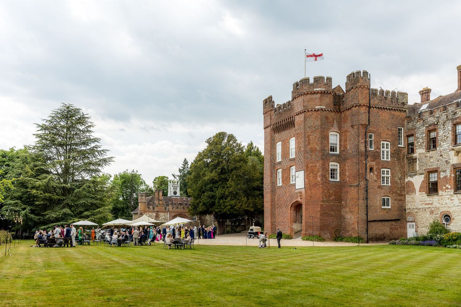 Historic castle with red brick tower hosting outdoor wedding reception on manicured lawn.