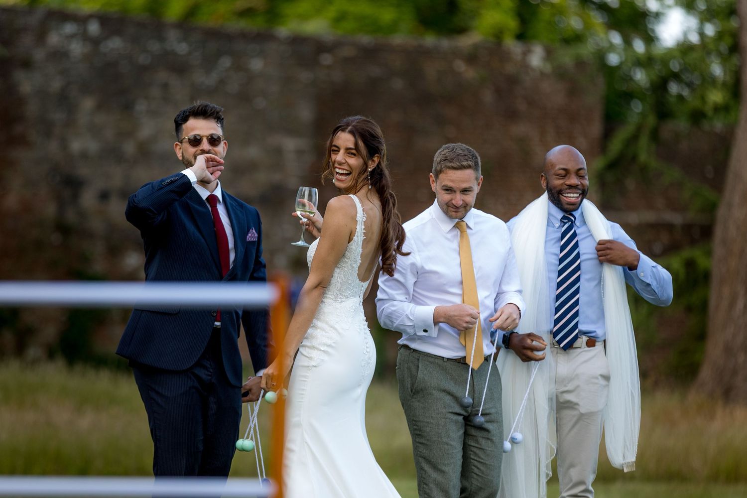Wedding guests mingle on lawn during outdoor reception near brick building.
