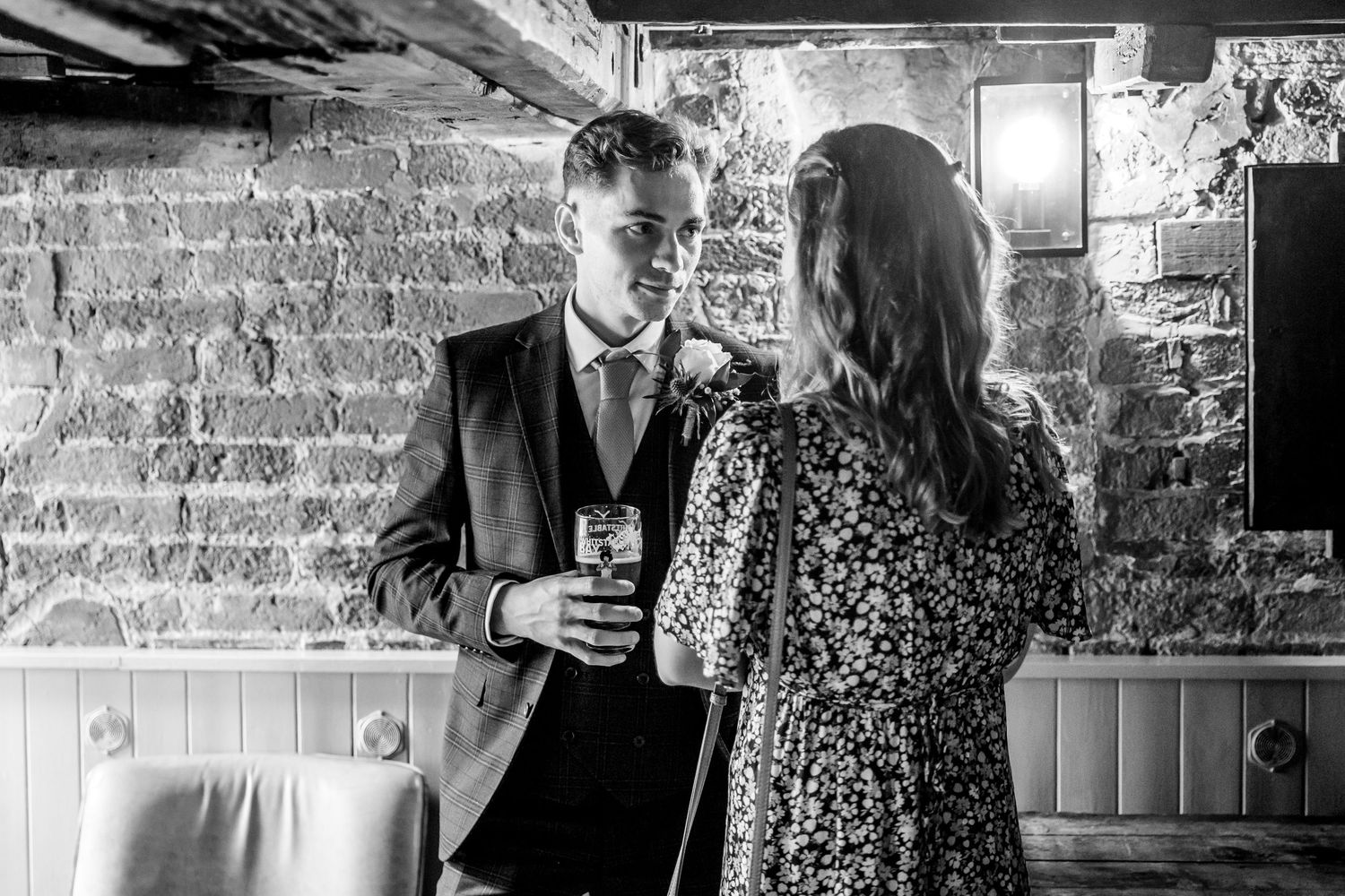 Guests mingle in rustic venue with exposed brick walls during social event.