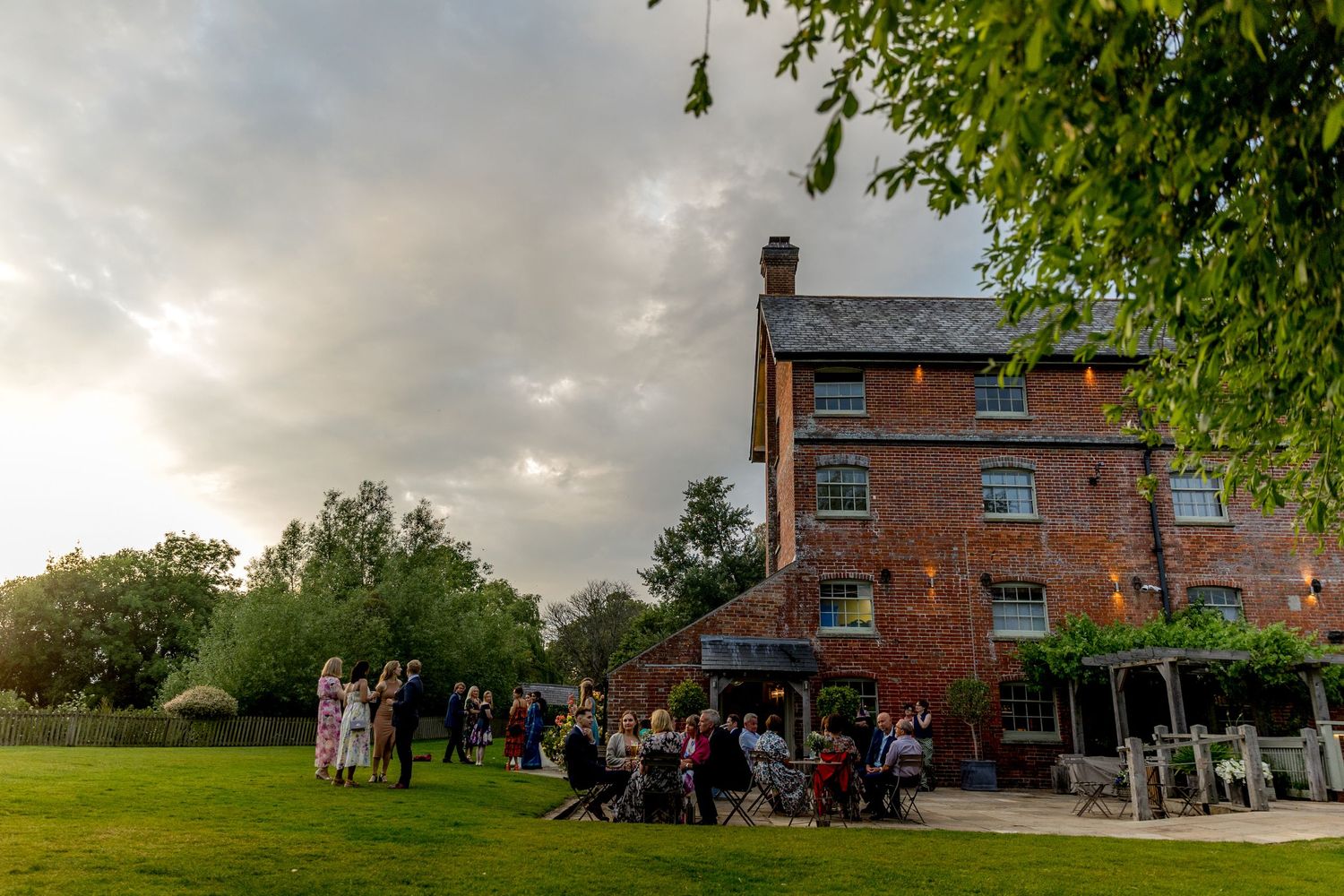 Exterior views of a brick wedding venue with guests mingling on the lawn at dusk.
