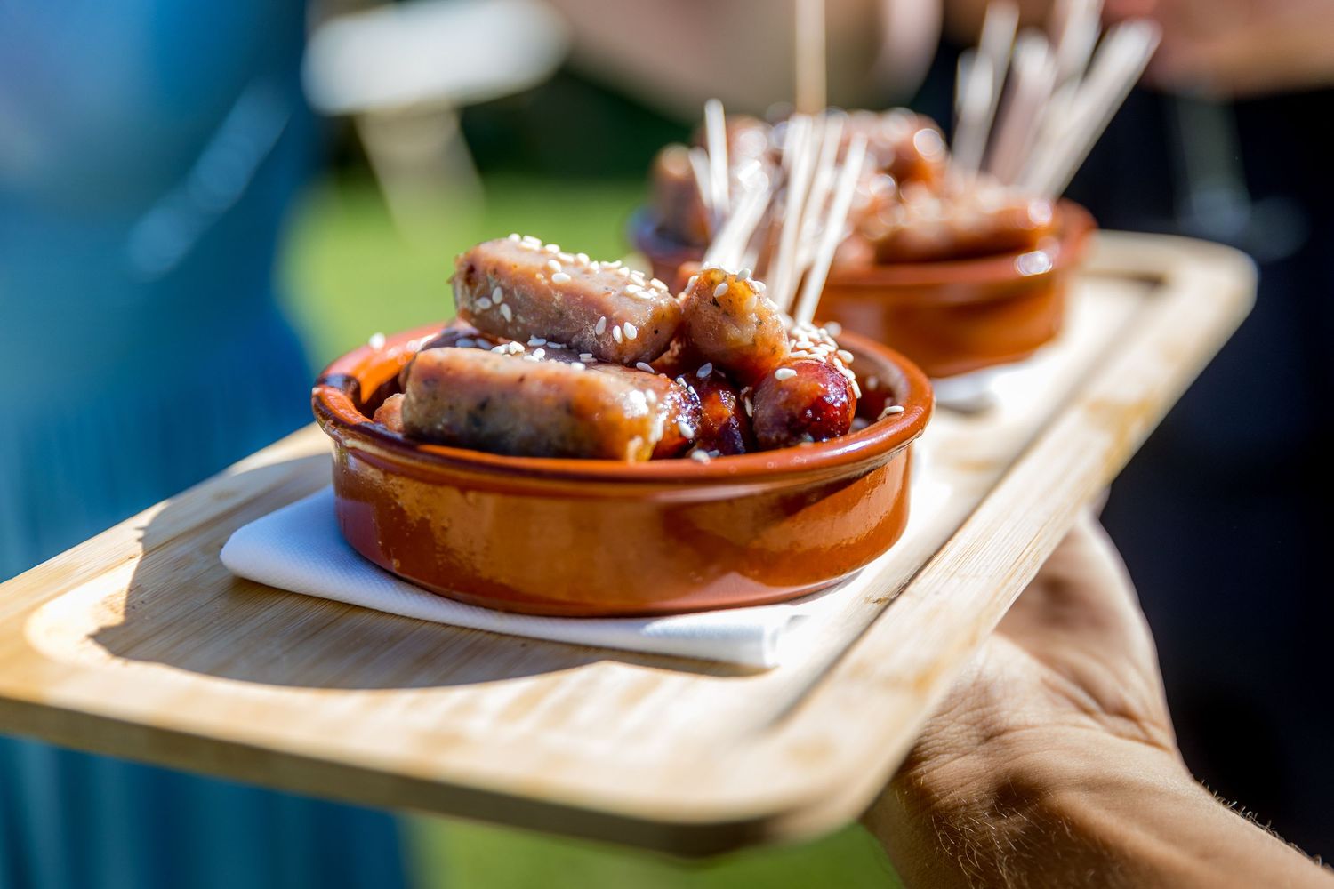 Wooden serving boards with appetizers being passed around at an outdoor event.