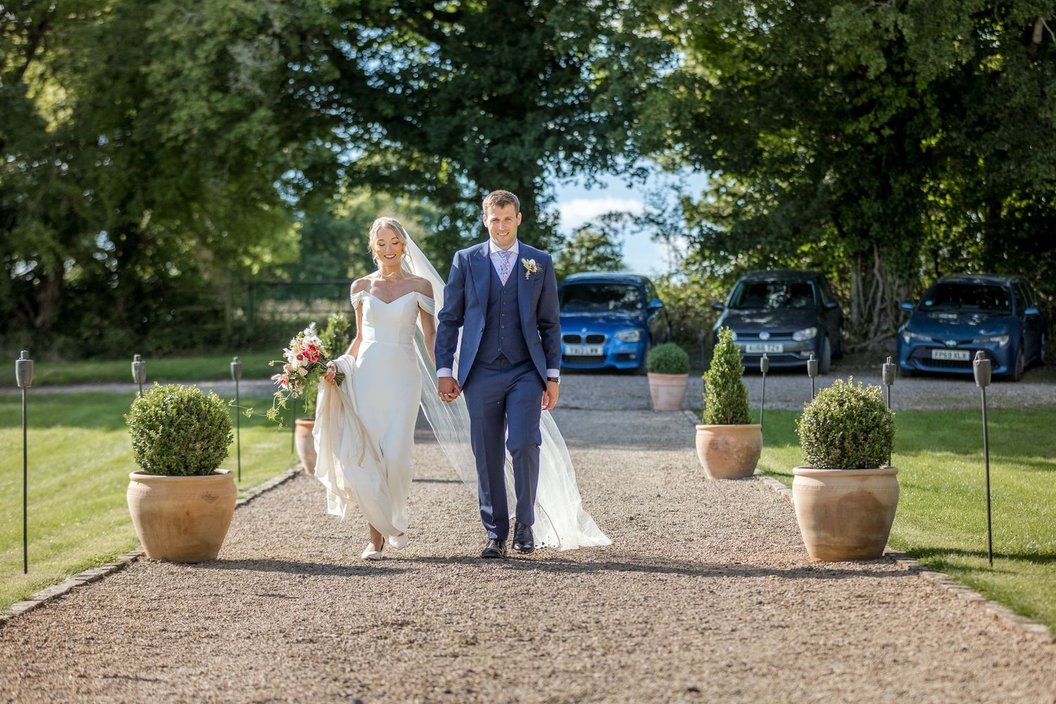 Wedding couple walking along a garden path with decorative potted plants.