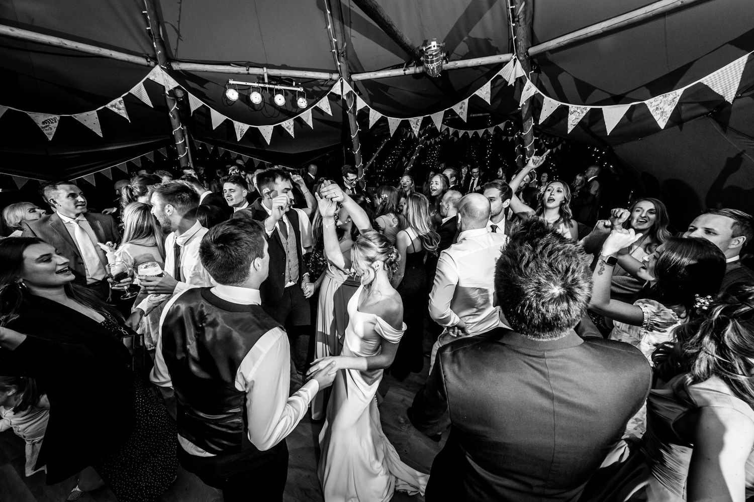 A black and white shot of wedding guests dancing and celebrating on a crowded dance floor.