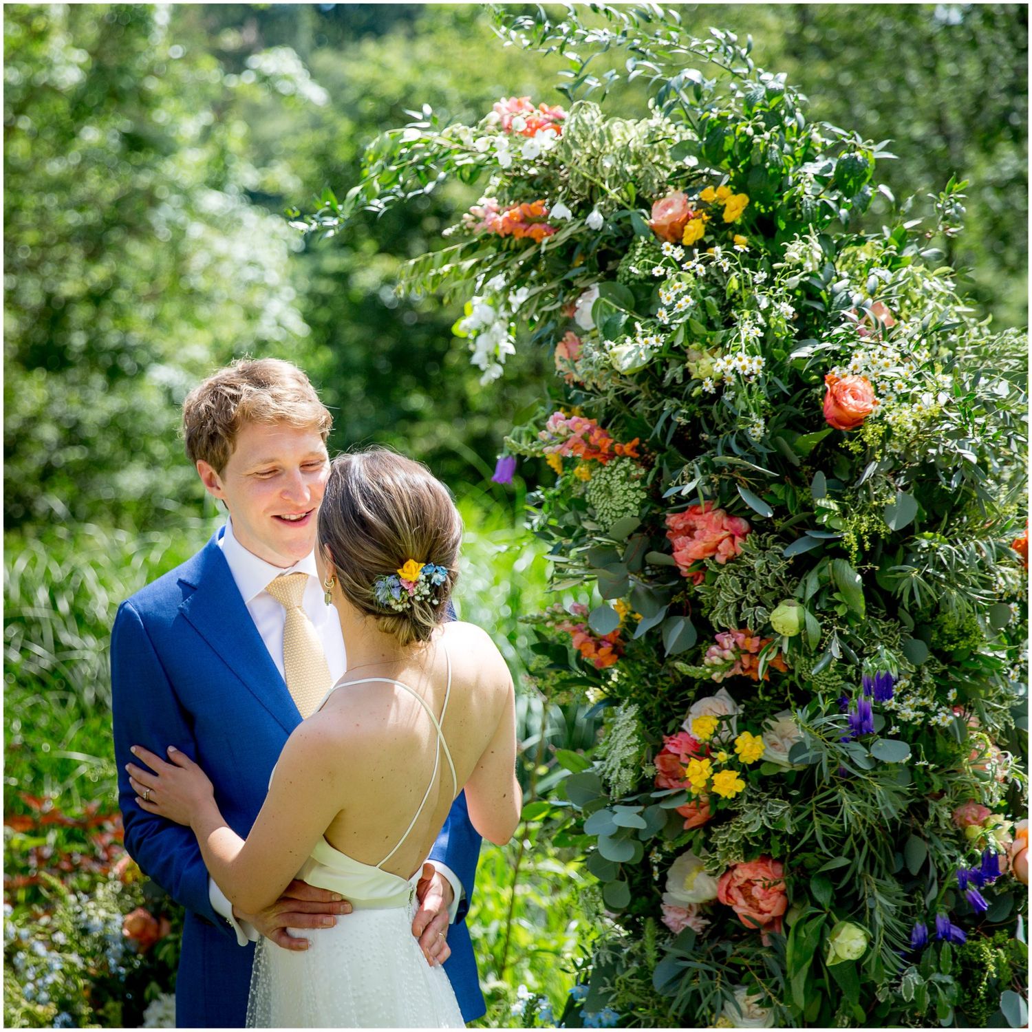 Wedding couple embraces near colorful floral arrangements in outdoor garden setting.