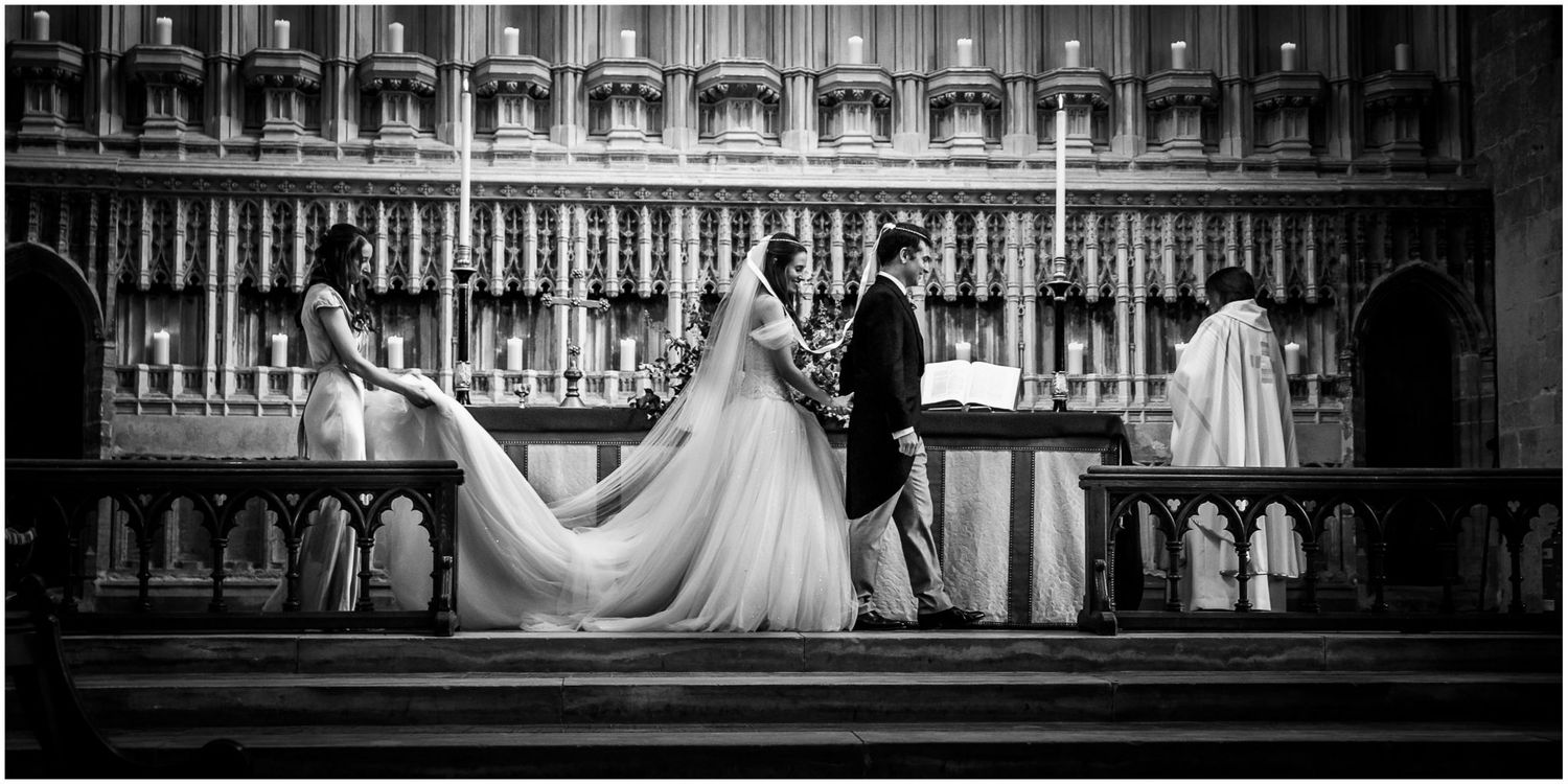 Elegant black and white wedding photograph on church steps with bride's flowing dress creating dramatic composition.