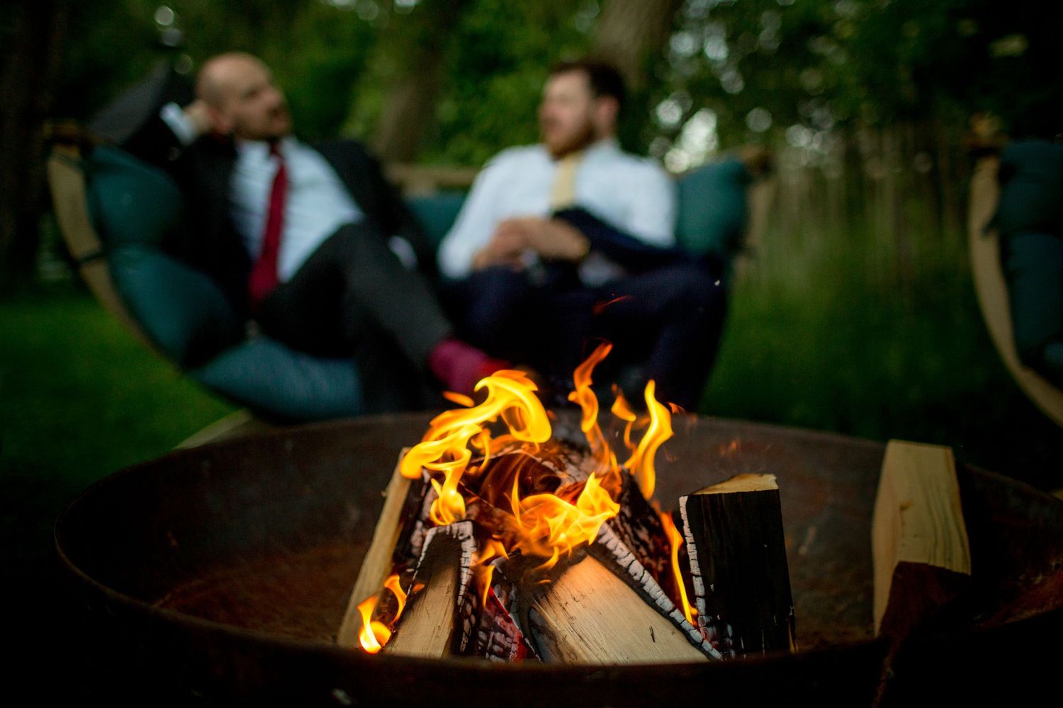 A warm campfire burns brightly in a metal fire pit as people gather around during an outdoor evening gathering.