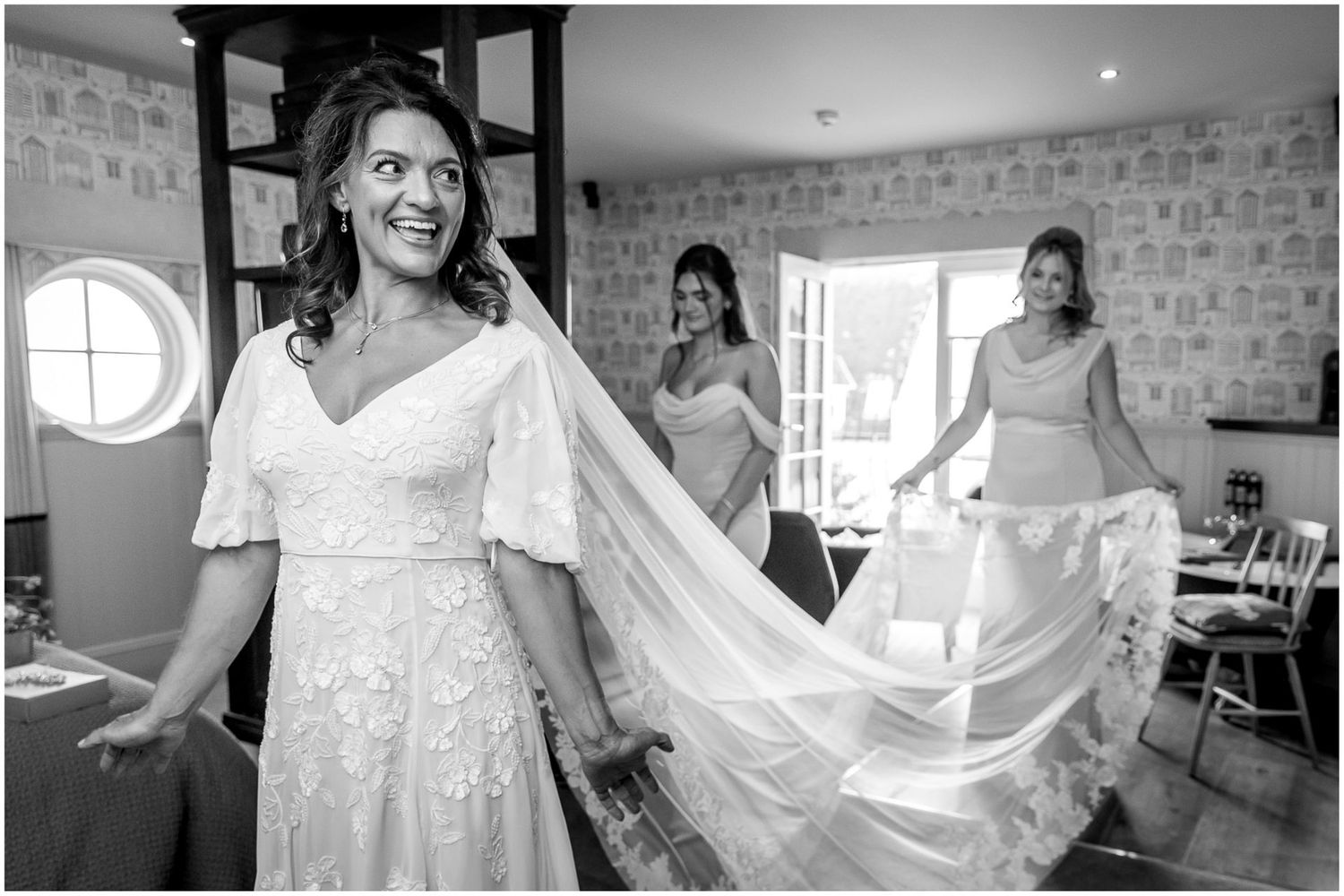 A joyful wedding preparation scene with a flowing veil in a bright brick-walled room.