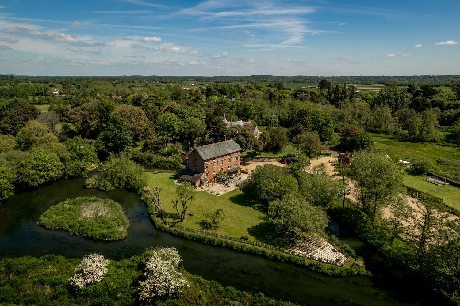 Aerial panoramic view of countryside estate buildings surrounded by green fields and trees.