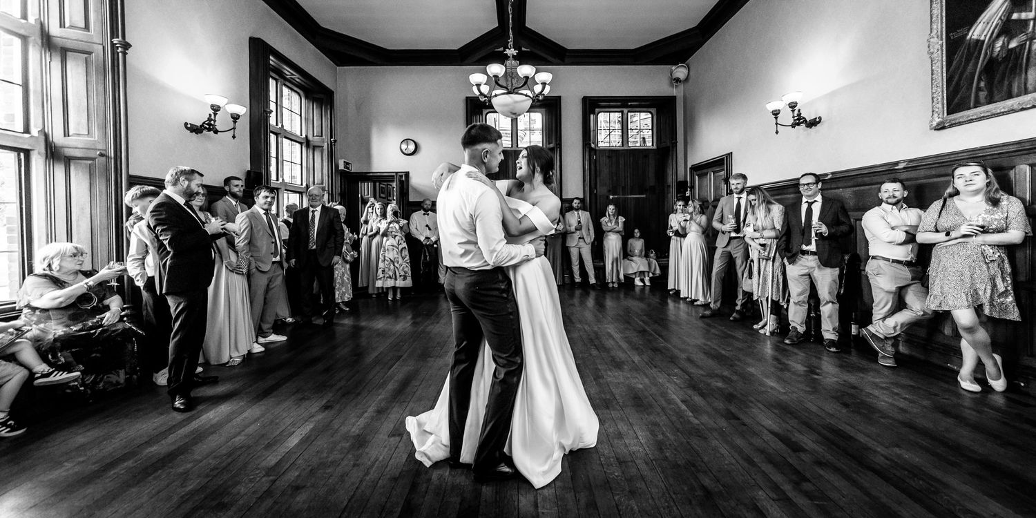 Black and white panorama of wedding reception festivities in an elegant indoor venue.