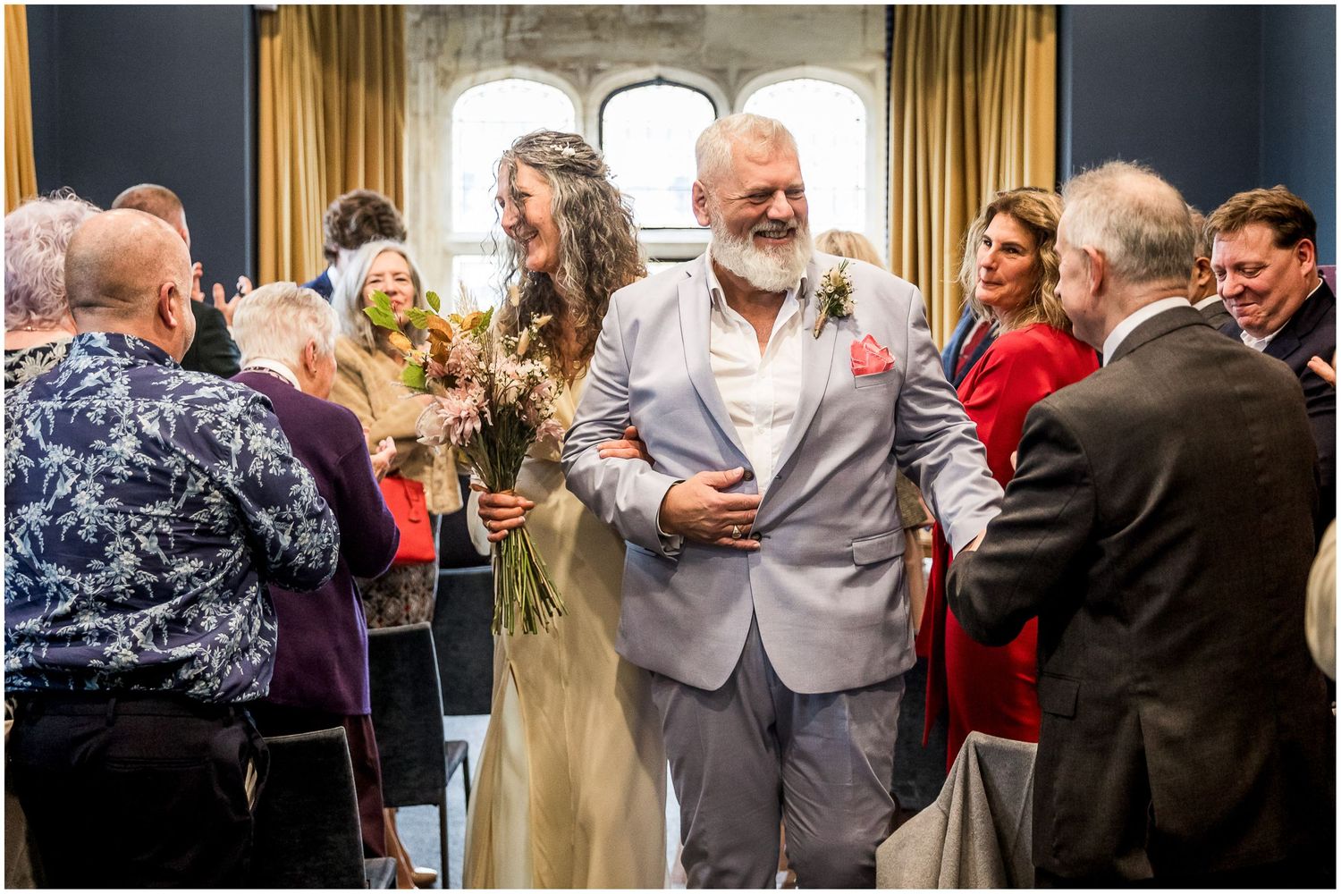 The bride and groom walk arm in arm together down the aisle of the Castle Room in Winchester