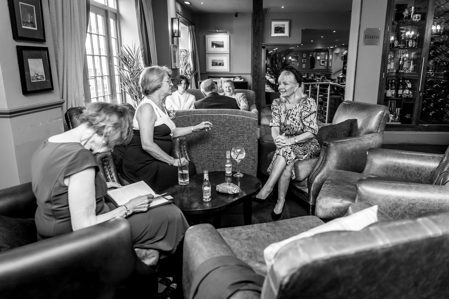 Black and white candid shots of wedding party socializing in an elegant room.