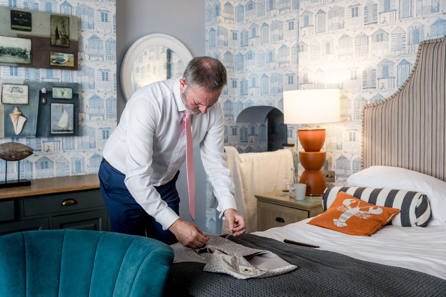 Elegant hotel room interior with blue velvet chair and patterned wallpaper featuring architectural sketches.